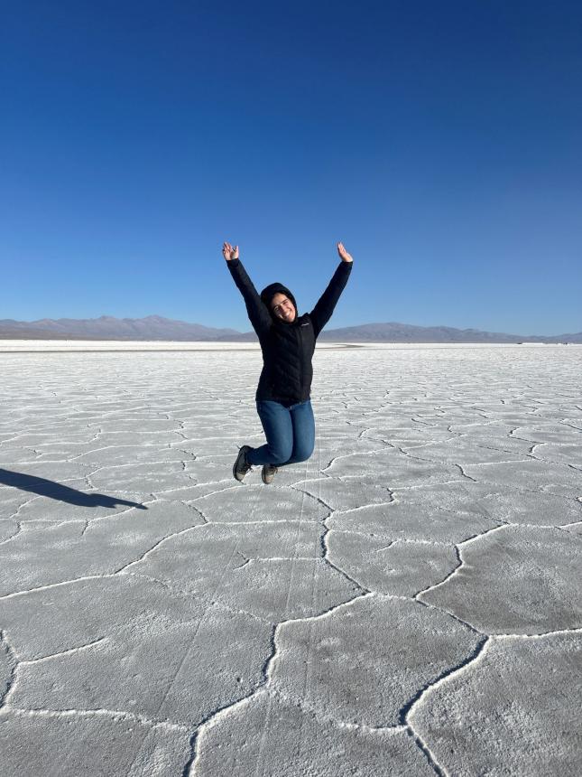 Girl wearing black jacket and blue jeans joyfully jumping with arms outstretched